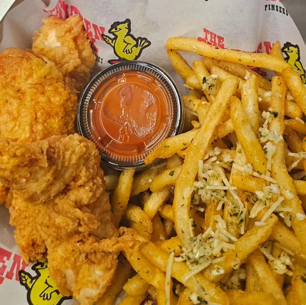 Chicken fingers with a cup of sauce and garlic fries